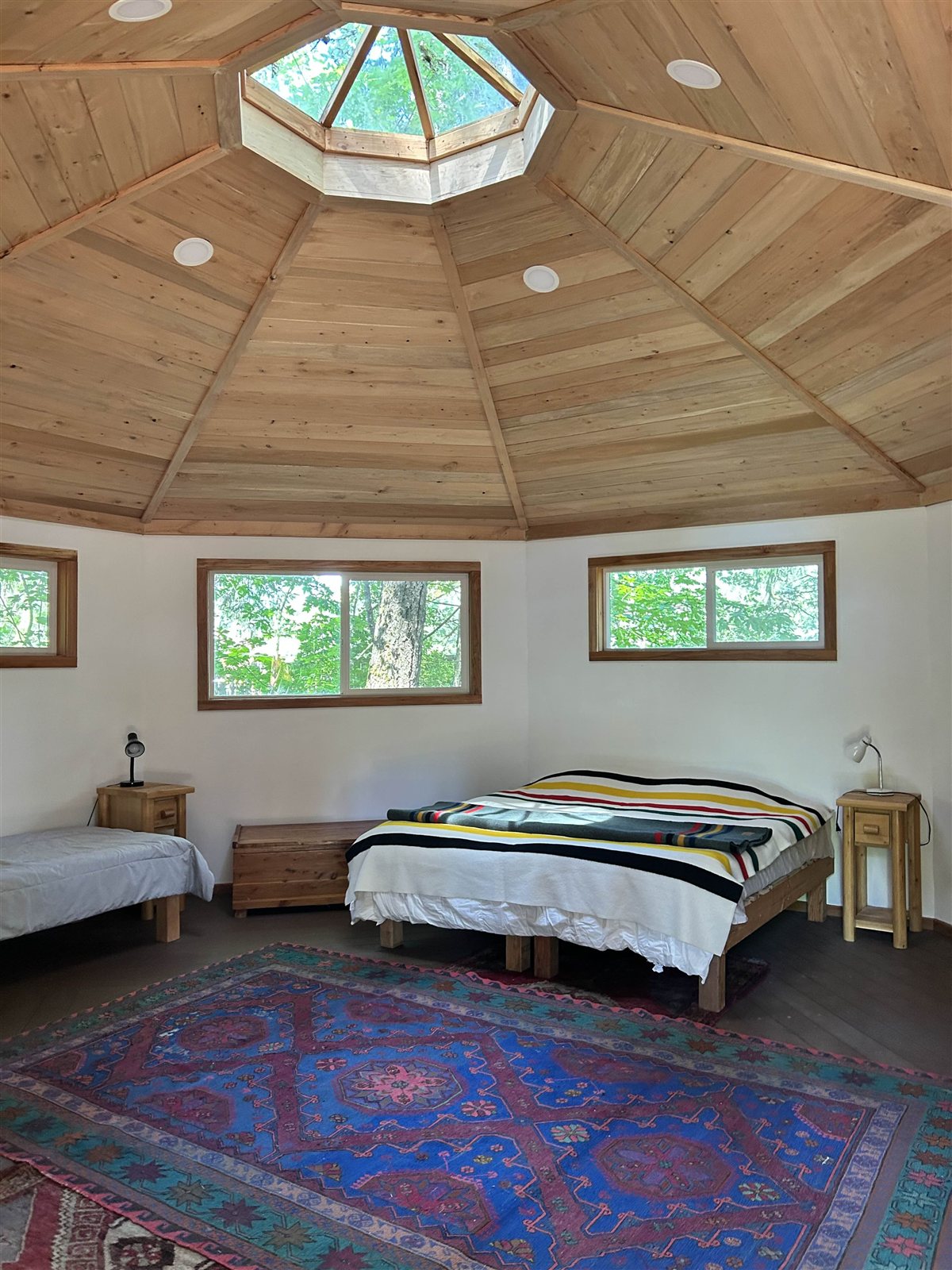 Round cabin interior with wooden dome ceiling, skylight, and cozy beds